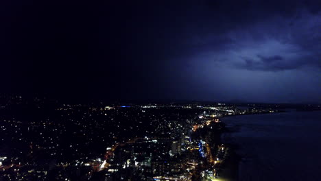 Toma-Aérea-En-Tiempo-Real-De-Una-Tormenta-Eléctrica-Sobre-Una-Ciudad-Costera-Por-La-Noche.