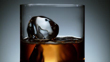 liquor being poured over ice cubes in a transparent glass