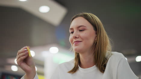 close-up of lady eating fries with warm smile, focused look, colorful lights blinking in background, enjoying snack in vibrant, casual dining setting with cheerful atmosphere