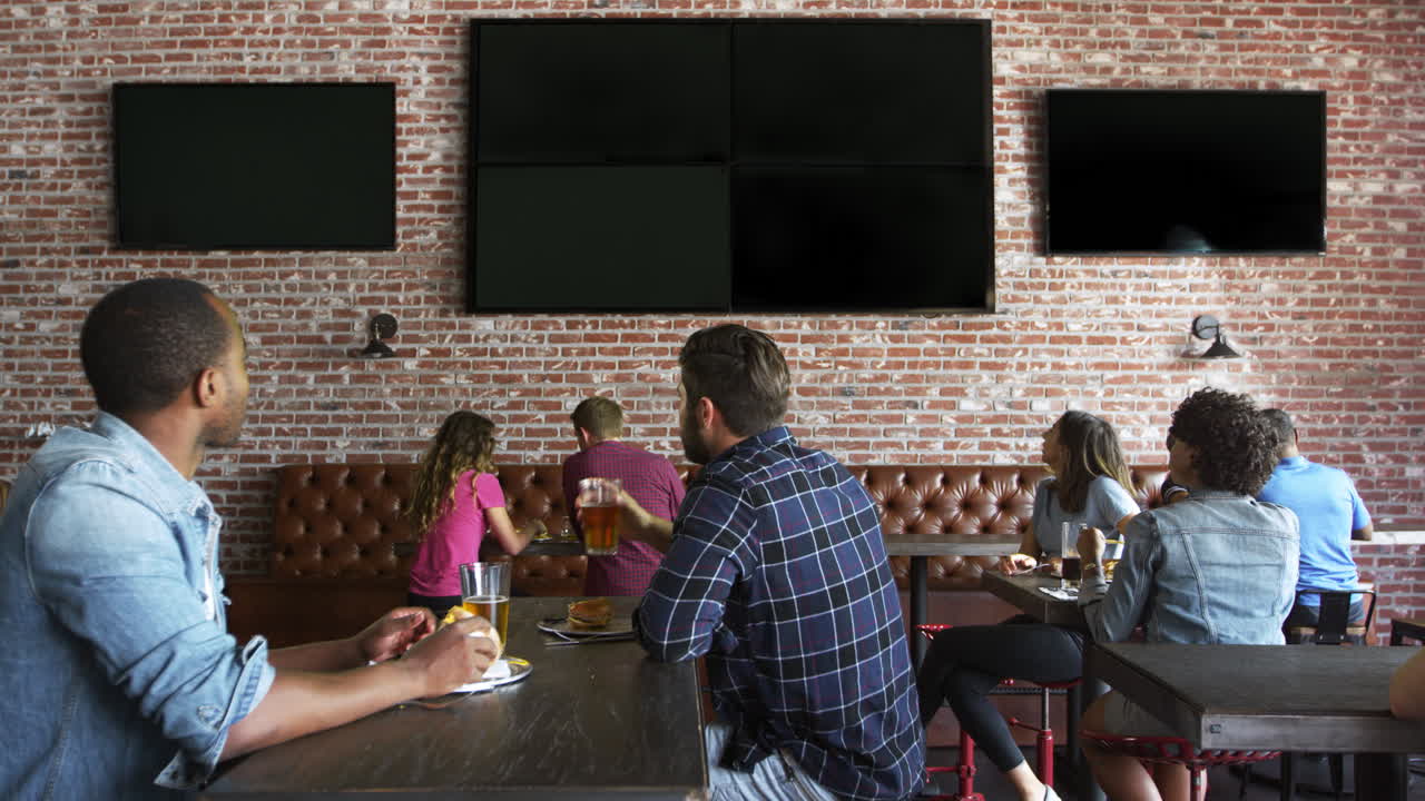 Amici che guardano una partita sugli schermi in un bar sportivo, ripresi con R3D.