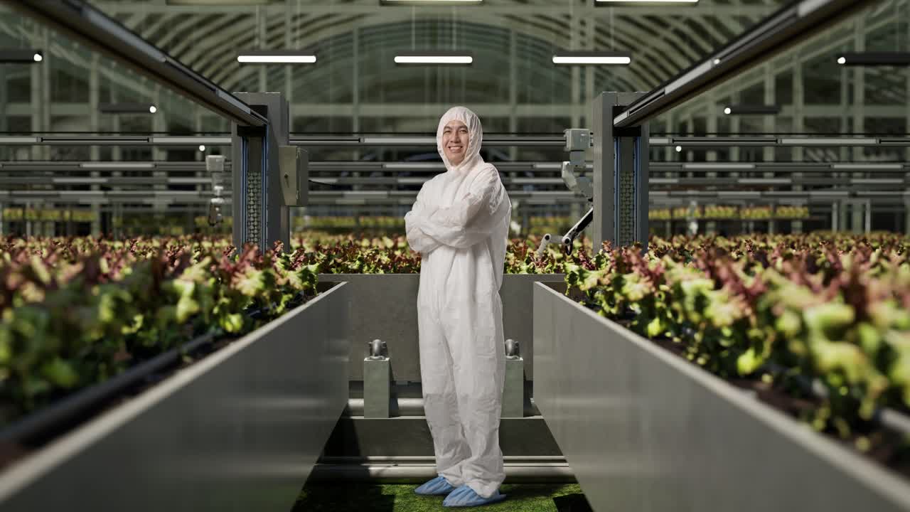Full Body Side View Of Asian Man Researcher Smiling And Crossing His Arms While Standing In The Greenhouse With Smart Robotic Farmers