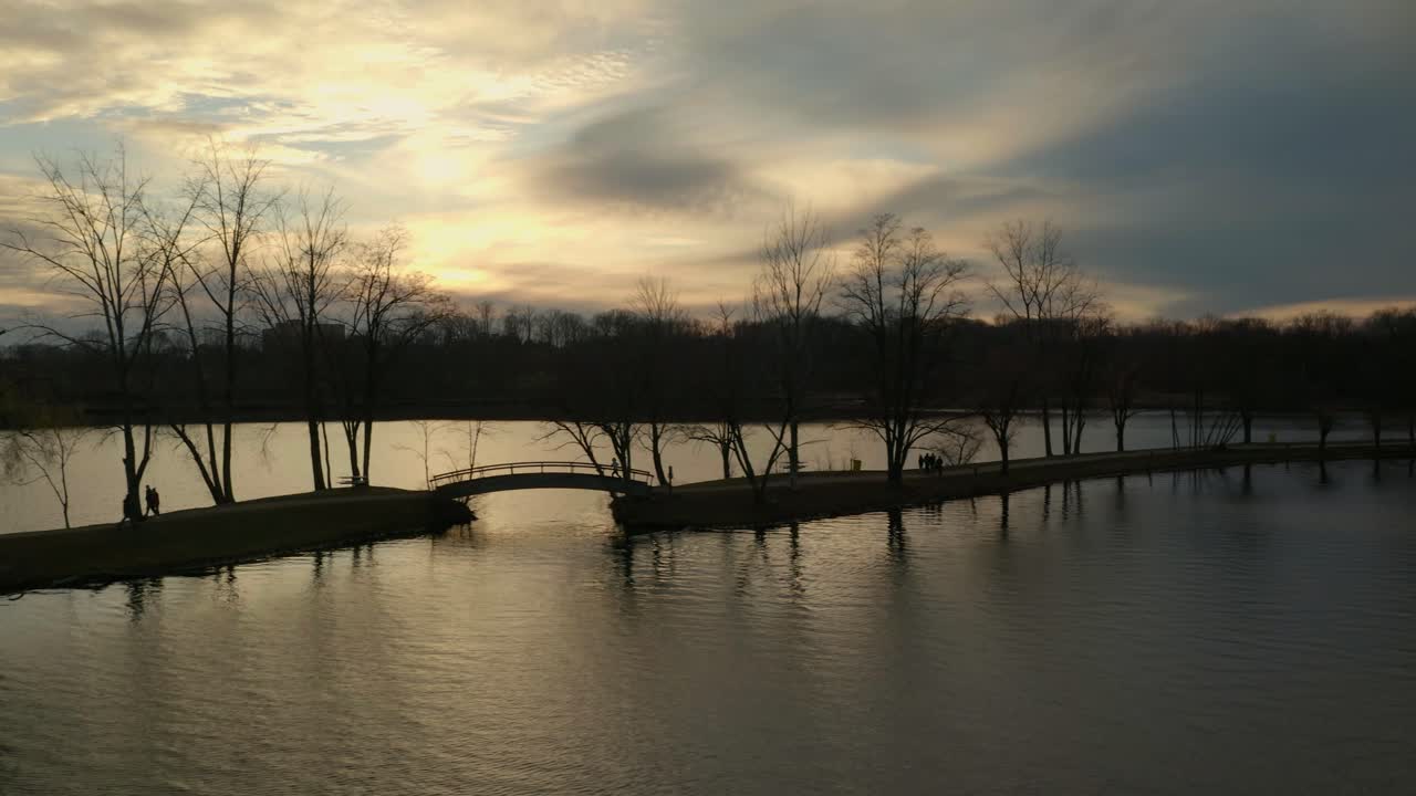 Sunset over a tranquil lake with silhouetted trees and a bridge