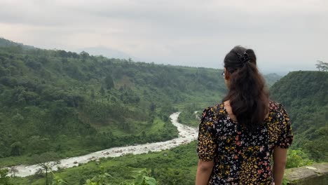 Rear-view-of-young-Indian-girl-watching-the-mountain-and-river-stream-at-hill-top-in-India-at-sunset