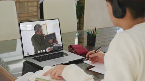 chico asiático usando computadora portátil para videollamada con profesor masculino en la pantalla