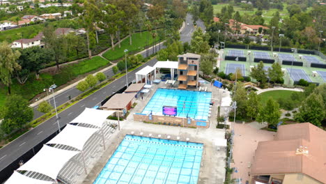 Aerial view of a recreational sports complex with multiple swimming pools and tennis courts amidst a green residential area