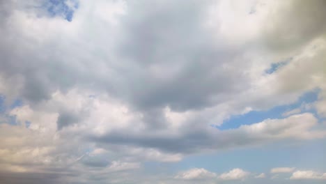 fluffy white and gray clouds moving across a blue sky lit with slivers of golden light.