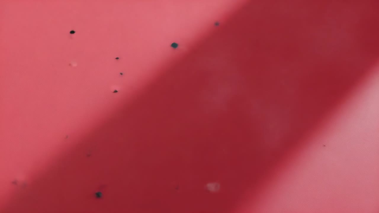 Shifting camera and light revealing specks, smudges and diagonal shadow on red panel studio closeup