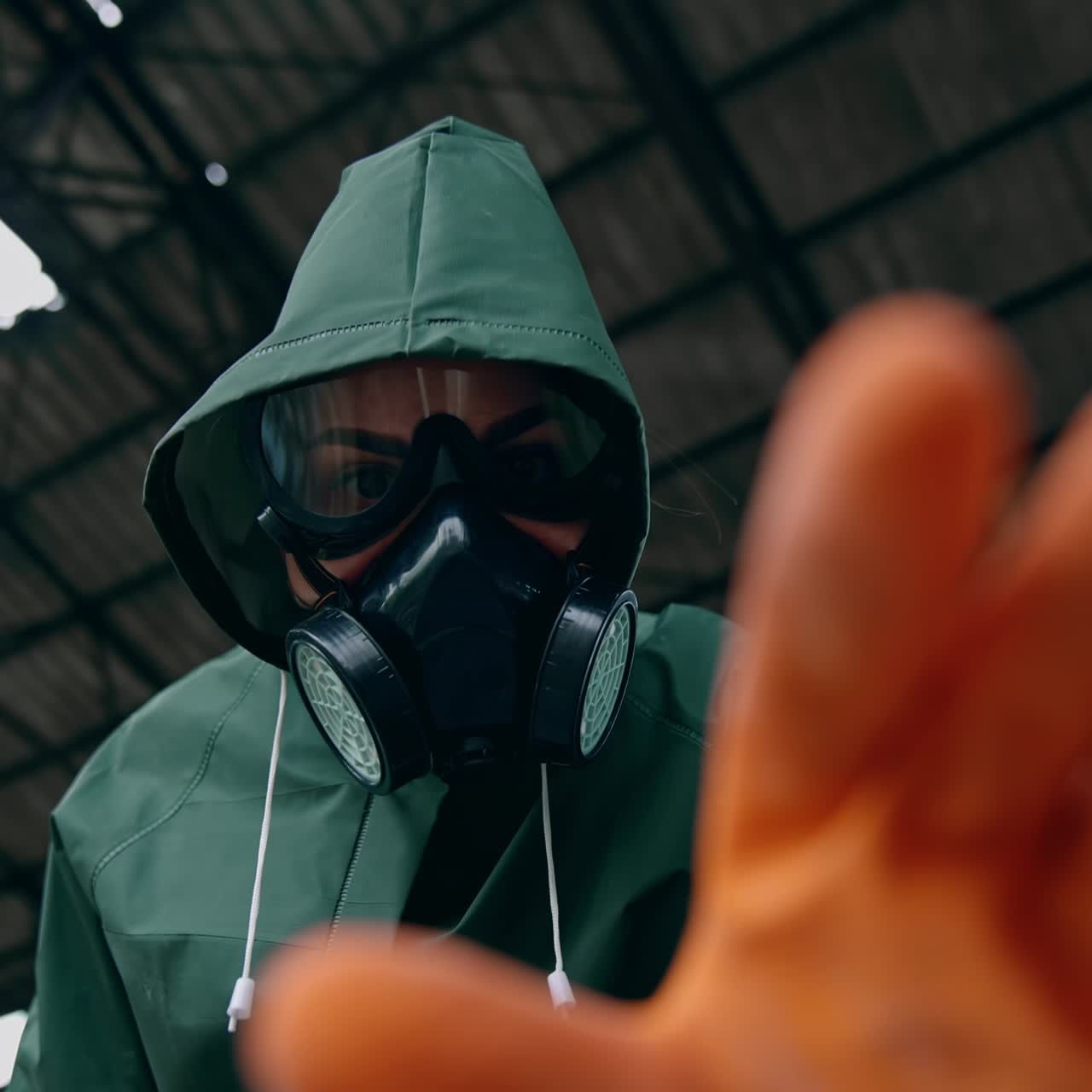 Portrait of a woman in safety suit and gas mask. Human wearing antibacterial costume trying to touch something with hand in glove in abandoned place. Gas attack