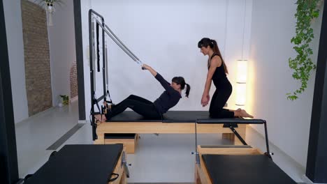 woman doing exercises on pilates reformer with instructor