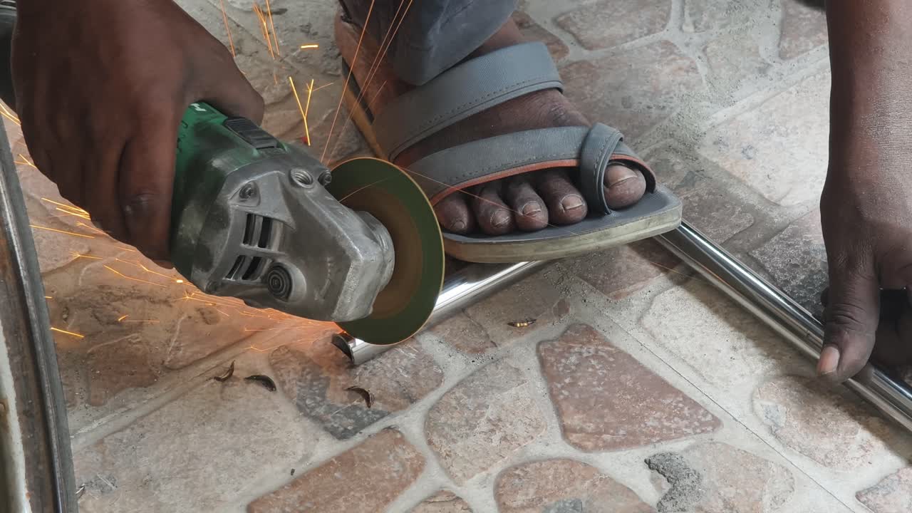 Closeup of a laborer using an electric angle grinder to cut a metal pipe on a tiled floor, creating bright sparks. Ideal for construction and industrial safety content