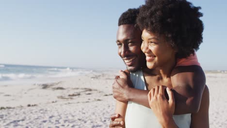 smiling african american couple embracing and looking away on sunny beach