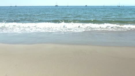 Cinematic-up-reveal-of-sandy-beach-and-small-waves-of-the-Pacific-ocean-with-boats-on-the-water-in-Santa-Barbara,-California,USA