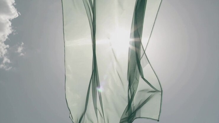 Fluttering green panel catching breeze, splitting into ribbons in sky, sun backlighting, left cloud