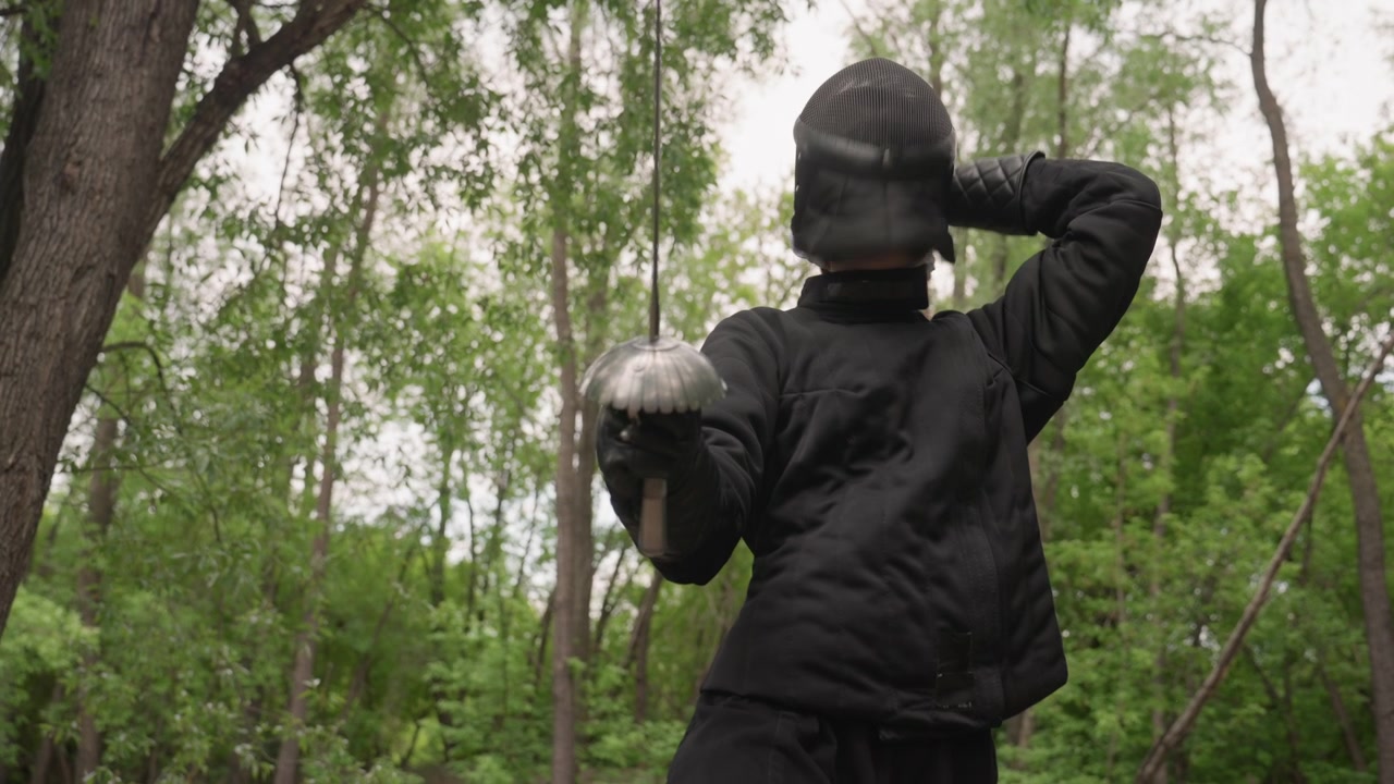 Close up of woman in black fencing gear holding and moving with sword outdoors. subject demonstrates various stances while wearing protective clothing including gloves