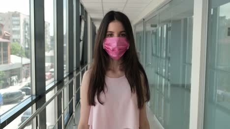 young woman wearing a pink mask walks through an office hallway