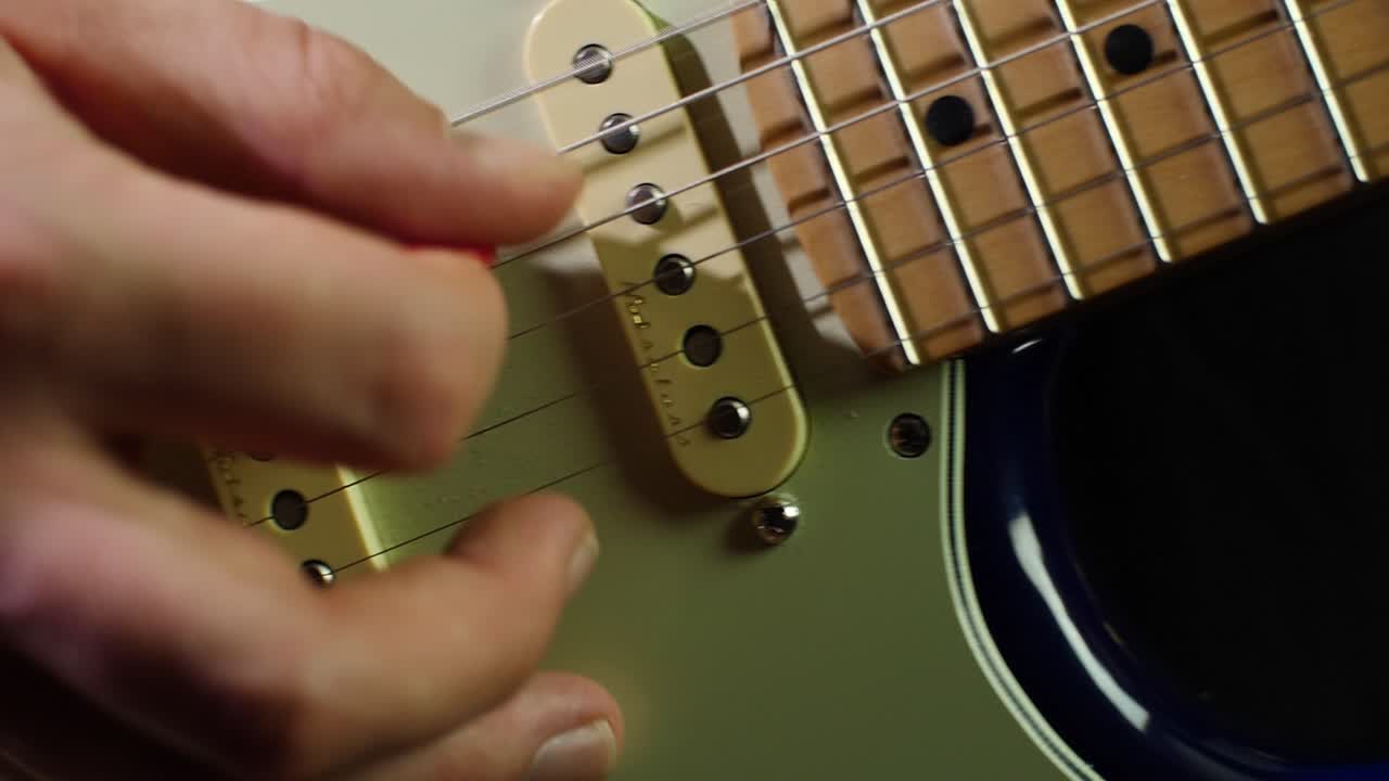 슬로우 모션은 전자 스트라토캐스터 기타의 목과 현, 기타리스트의 손을 닫고 피크로 음을 연주하는 동안