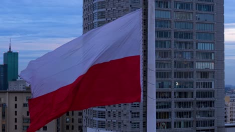 slow motion aerial orbit of polish flag waving in strong wind, warsaw cityscape in the background