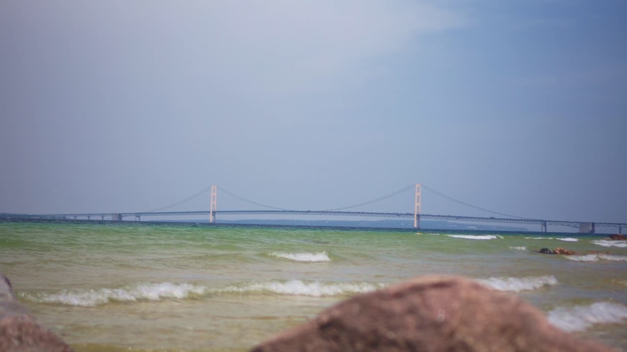 Wide Tilt Up Shot of Mackinac Bridge in Michigan with Rocks and Waves in Foreground