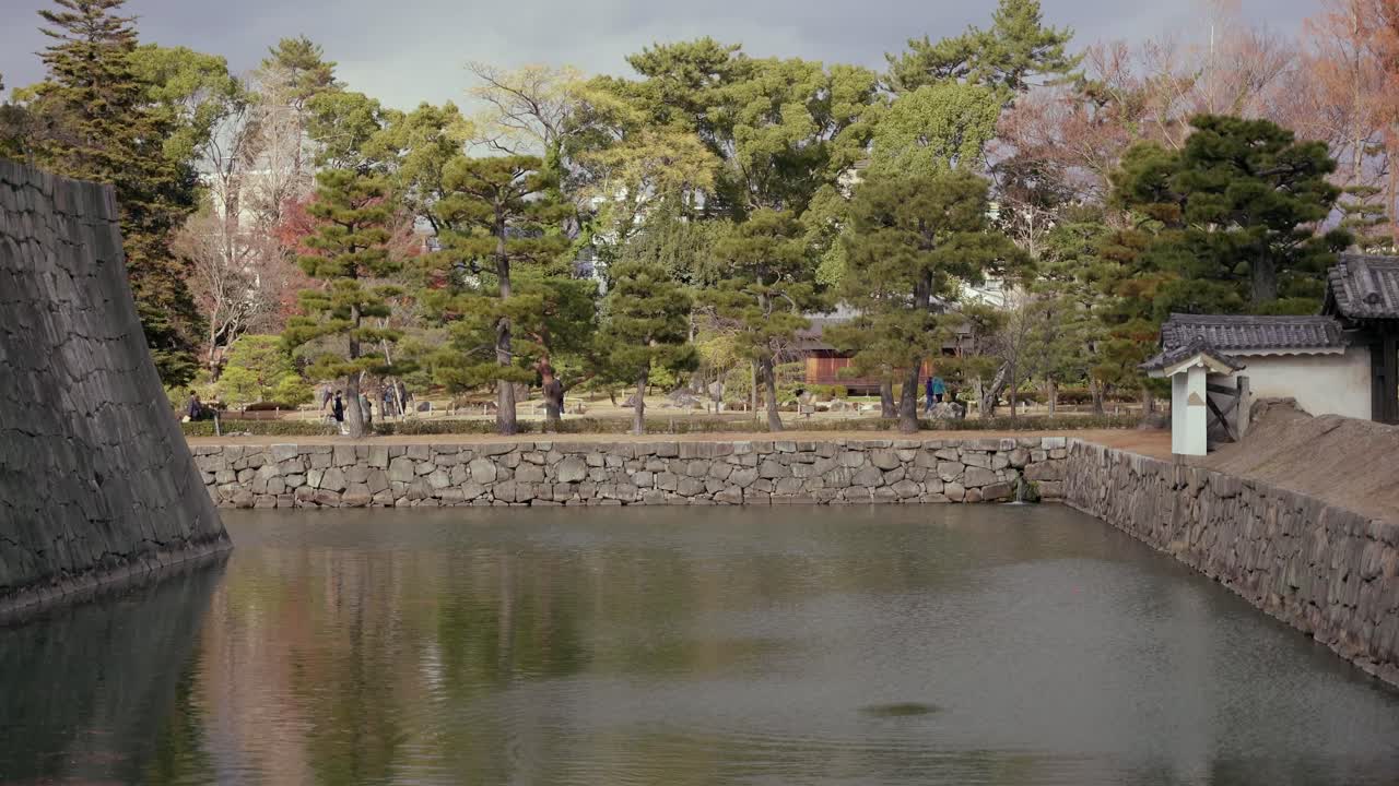 View across the moat at Nijō Castle in Kyoto, Japan. There are tourists walking on the other side of the moat
