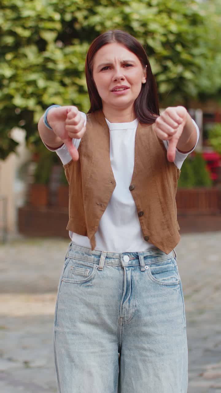 una joven caucásica molesta muestra dos pulgares hacia abajo expresando su descontento en la calle de la ciudad.