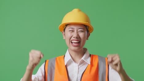 close up of asian female engineer with safety helmet screaming goal and dancing celebrating in the green screen background studio