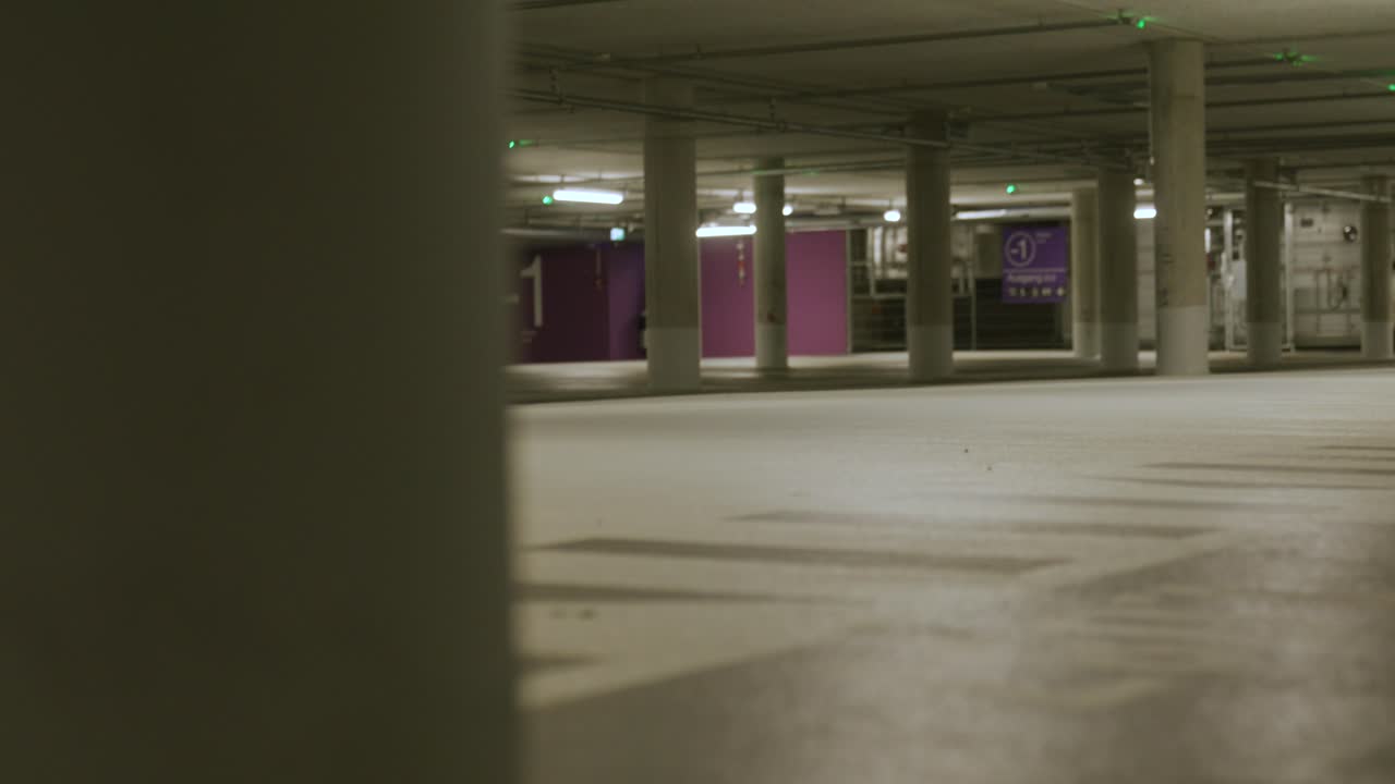 View of black male walking in across screen into empty underground parking lot with bright lights in Metzingen, Germany, Baden Wurttemberg, Europe, panning view angle