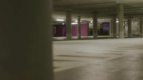 view of black male walking in across screen into empty underground parking lot with bright lights in metzingen, germany, baden wurttemberg, europe, panning view angle