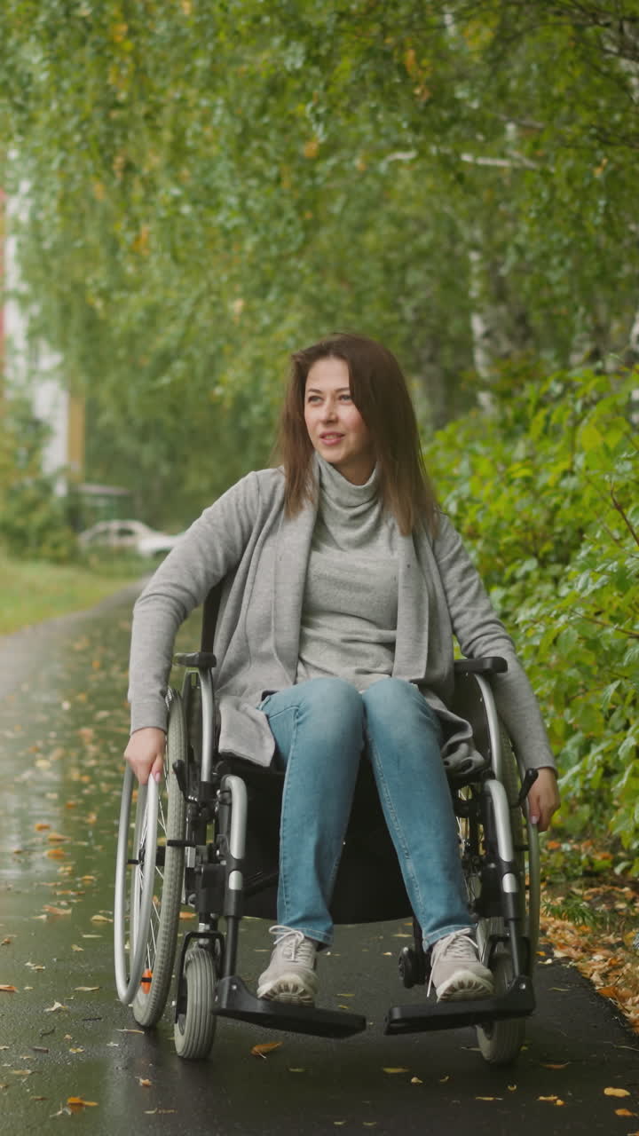 joven con discapacidad gira grandes ruedas de silla de ruedas moviéndose a lo largo de un camino en un jardín público verde. recuperación de la salud después de una lesión en el complejo