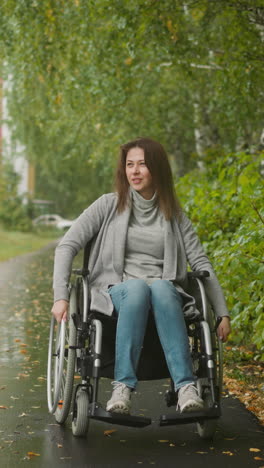 joven con discapacidad gira grandes ruedas de silla de ruedas moviéndose a lo largo de un camino en un jardín público verde. recuperación de la salud después de una lesión en el complejo