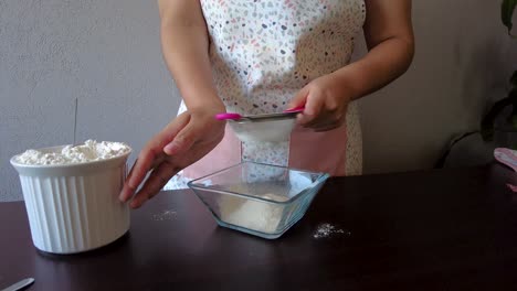 latin woman wearing an apron preparing cooking baking a cake sieving the flour with a metal strainer