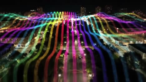 a stunning aerial view of a cityscape illuminated by vibrant light patterns in a nighttime spectacle, showcasing colorful waves and architectural beauty