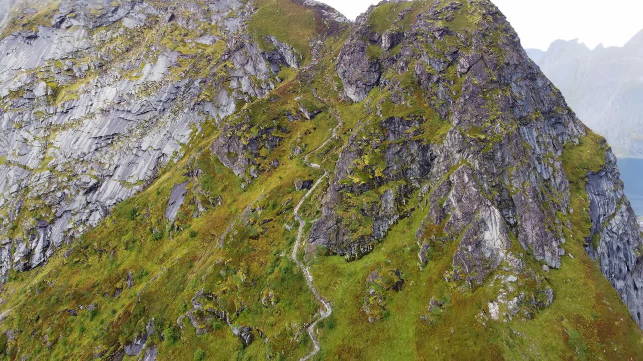 camino a la montaña escarpada rodeada por el mar en el norte de noruega con gente subiendo escaleras hasta la cima filmada por drones