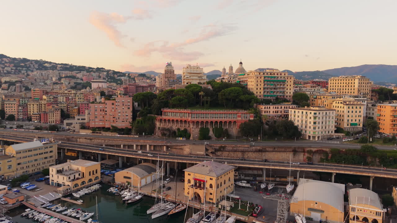 Drone shot of Genoa port in Italy at sunset, boats, colorful buildings, traffic on highway and scenic urban skyline