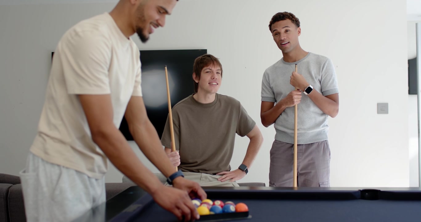 Diversos amigos masculinos colocando las bolas en la mesa de billar azul en la sala de juegos, quitando el triángulo, preparando el tiro de salida