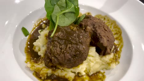 a comforting dish featuring tender meat served with a rich sauce over a bed of creamy mashed potatoes, garnished with fresh spinach. a hearty and flavorful meal showcasing classic flavors and textures