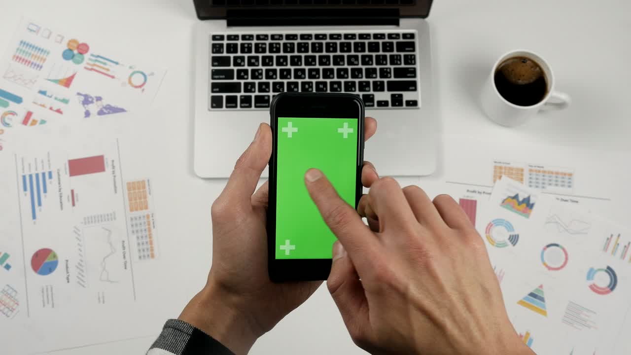 hombre de negocios usando un teléfono inteligente con pantalla verde en el fondo blanco de la mesa de la oficina. vista superior. manos masculinas desplazando páginas, zoomando, tocando la pantalla táctil. fondo de escritorio de la oficina