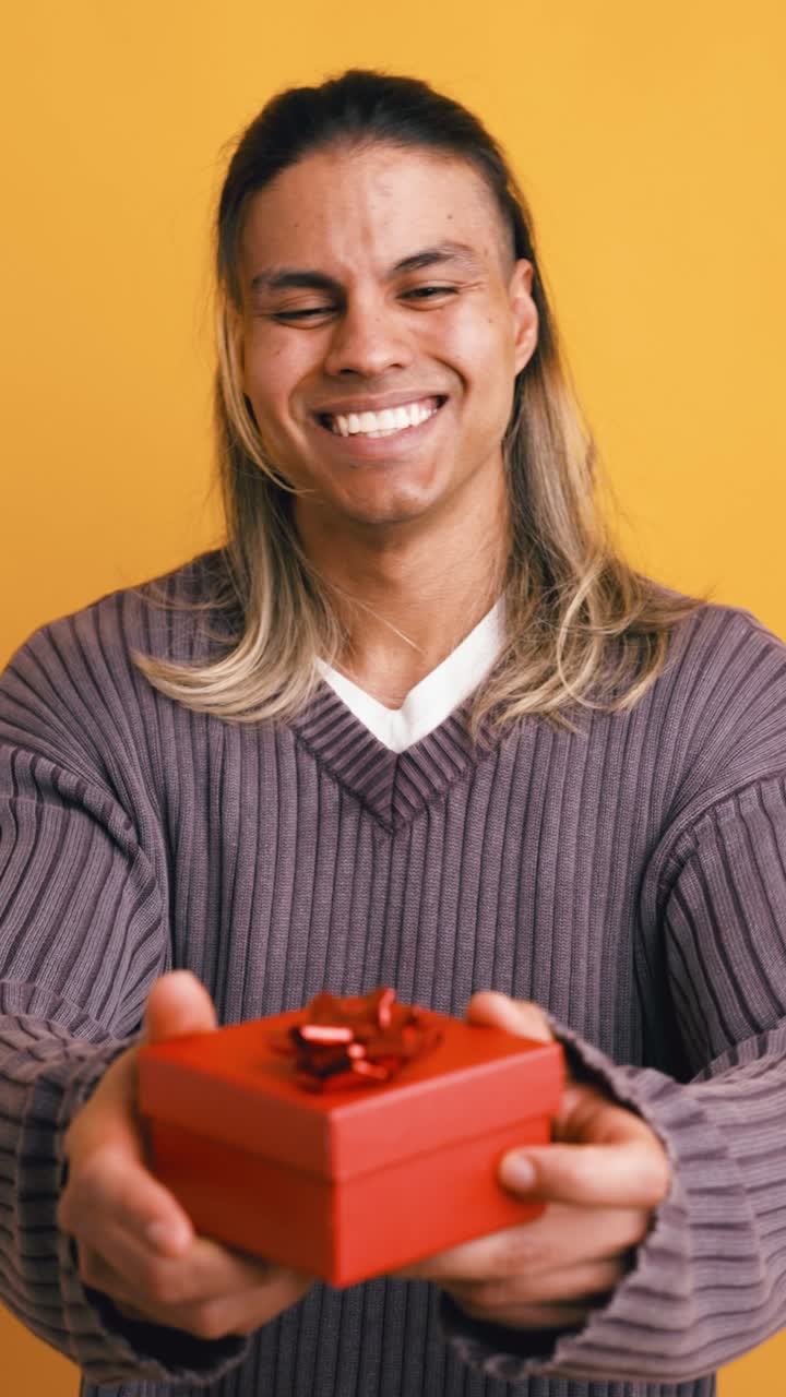 Giovane uomo sorridente che tiene in mano e presenta una scatola regalo rossa