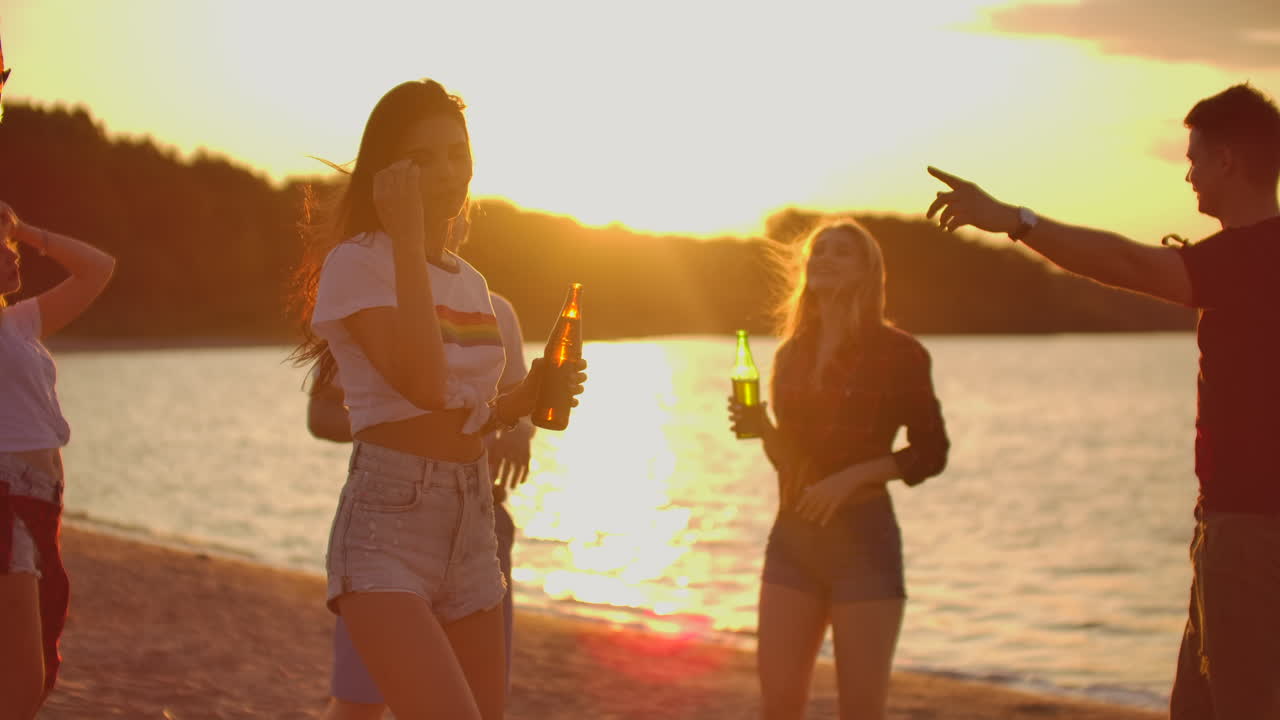 The young girl with dark hair is dancing with slim nude waist on the open air party with beer. It is crazy and hot beach party with the best friends in the good mood.