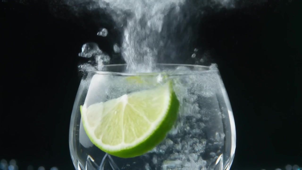 Fetta di lime che cade in un bicchiere di acqua frizzante