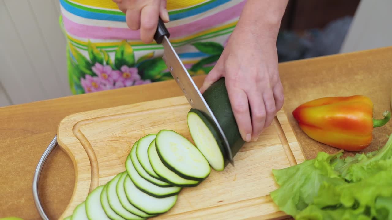 Women's hands Housewives cut with a knife fresh zucchini on the cutting Board of the kitchen table