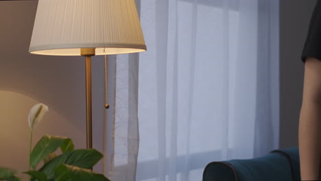 Junge-Frau-Schaltet-Abends-Im-Wohnzimmer-Eine-Stehlampe-Ein.-Detailaufnahme-Des-Interieurs-Und-Der-Möbel-Eines-Gemütlichen-Apartments