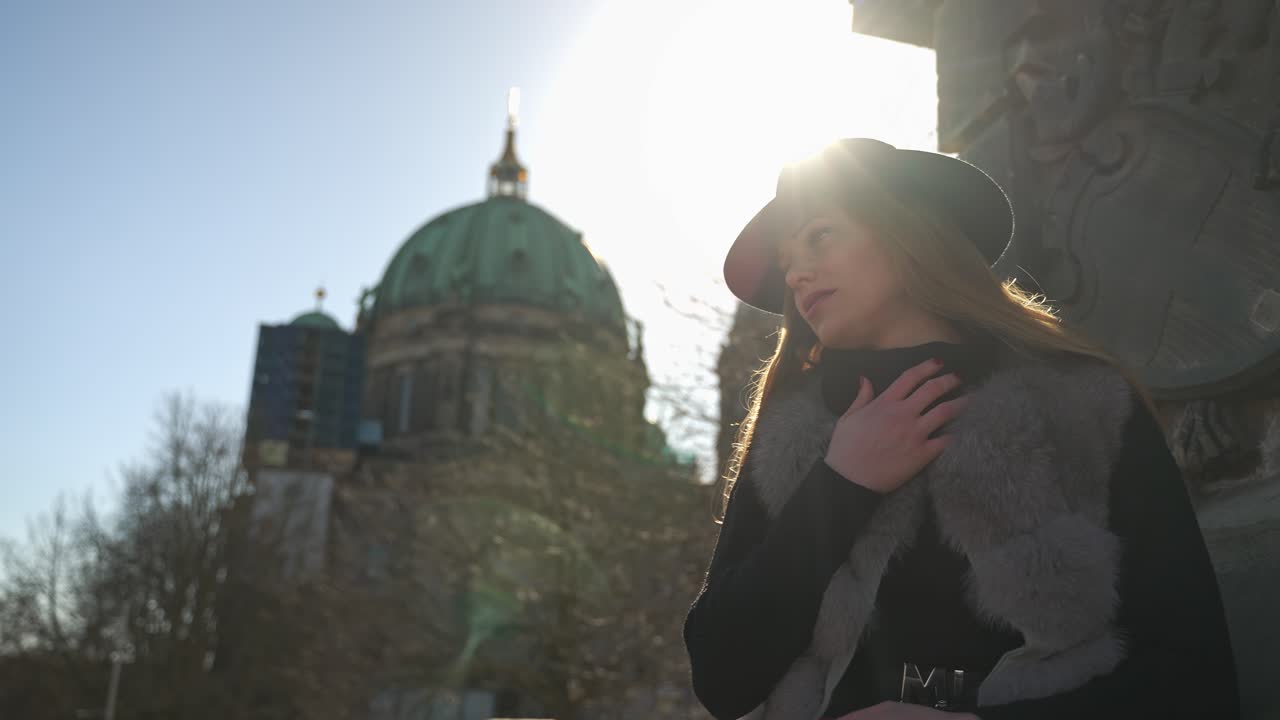 밝은 태양과 베를린 대성당을 배경으로 사진 촬영을 위해 야외에서 포즈를 취하는 모자를 쓴 아름다운 금발 여성