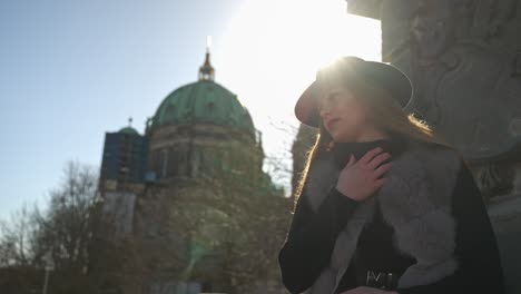 beautiful blonde woman in hat posing outdoors for photoshoot against bright sun and berlin cathedral