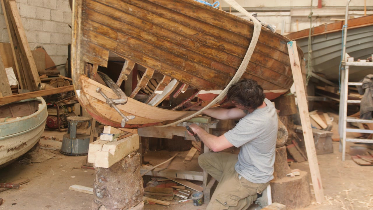 Giovane uomo che fissa le assi dello scafo di una barca in legno a clinker