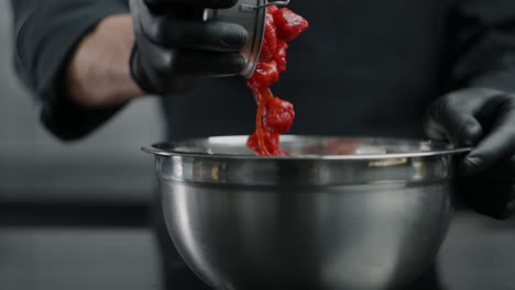 chef pouring red food into a metal bowl