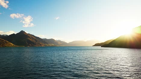 Aerial-pullback-with-mountains-and-sun-ray-retreating-behind-silhouette-of-forest