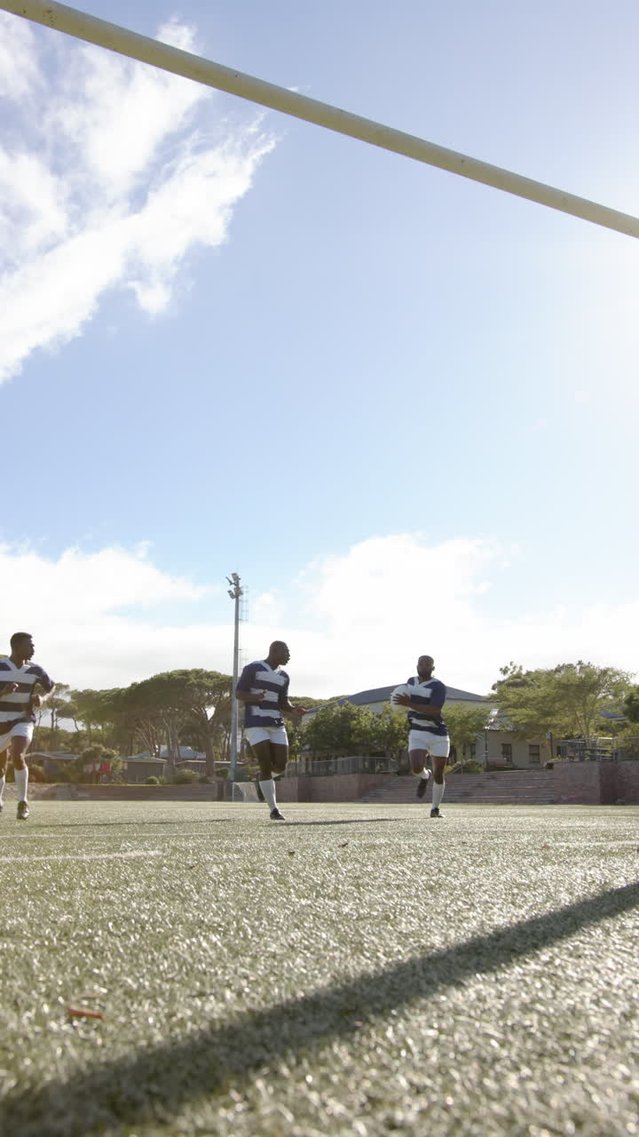 Vertical video: Rugby players running on field, holding ball, training under clear sky