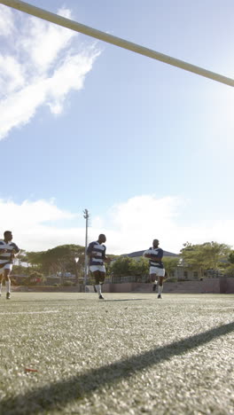 vertical video: rugby players running on field, holding ball, training under clear sky