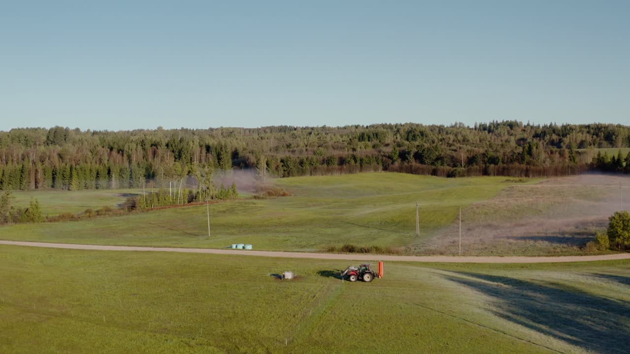 Drone side follow shot of a tractor in a field. Verdant countryside farmland.