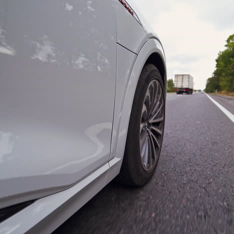 close-up view on the side part of a car and a wheel at moving the road. wheel of luxury white car turning slowly on asphalt road.